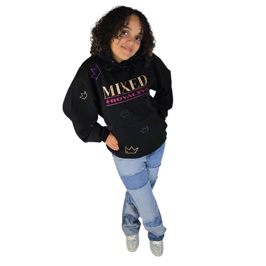 Smiling mixed-race girl wearing a black 'Mixed Royalty' hoodie with gold and purple sparkle lettering and sparkle crowns randomly all over with patchwork jeans, and sparkly sneakers.  Youth empowerment fashion promoting biracial pride.