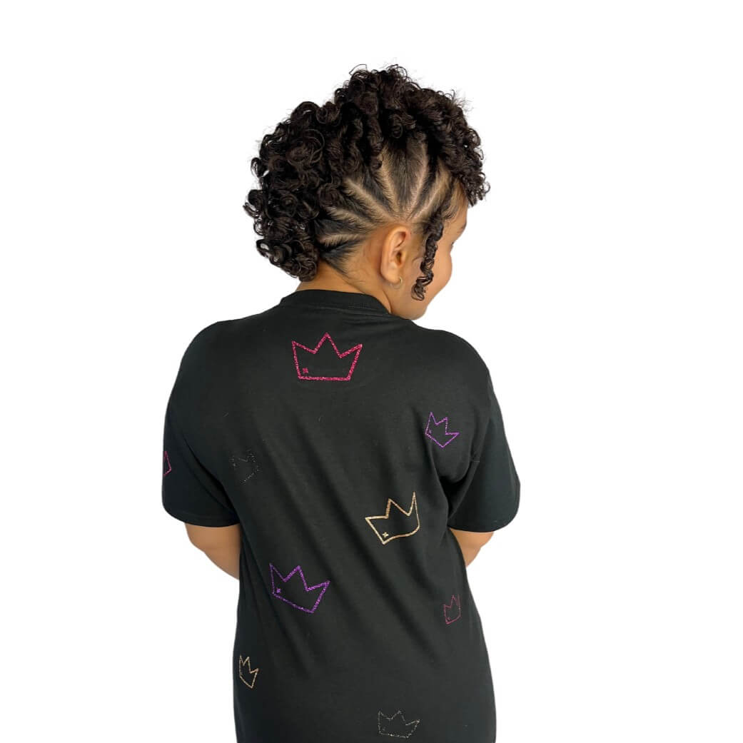 Child wearing Uniquely Mixed black crown-patterned t-shirt with braided curly hairstyle, representing inclusive kids fashion and modern streetwear style on white background.