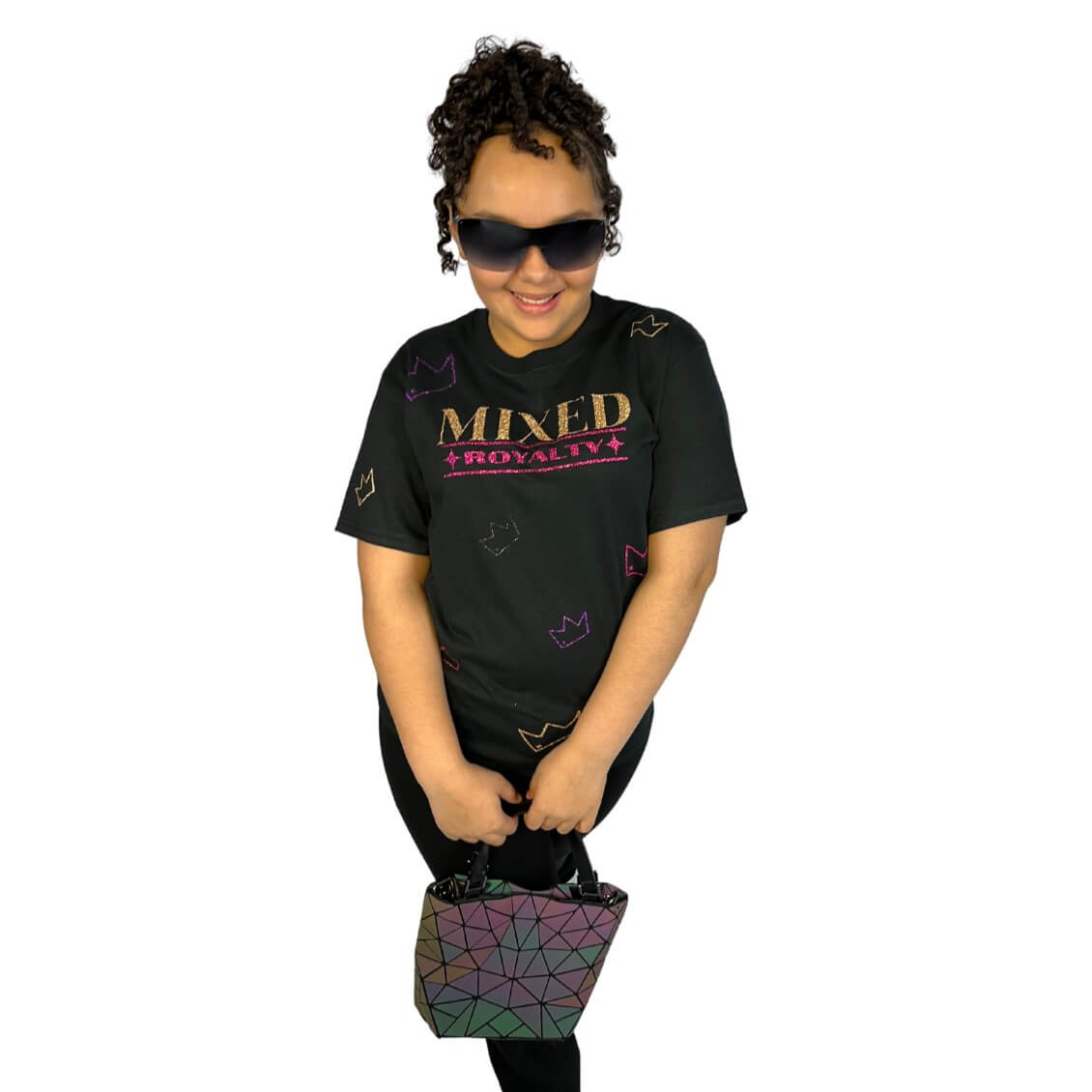 Child with curly hair wearing a black t-shirt with 'MIXED ROYALTY' text and crown sparkly pattern, holding a colorful geometric bag on a white background